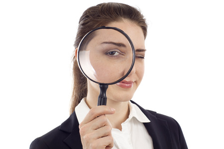 Confident young woman looking through a magnifying glass isolated over white backgroundの写真素材