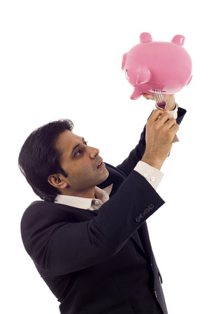 Desperate Indian businessman trying to take money out of a piggybank with a fork isolated over white backgroundの写真素材