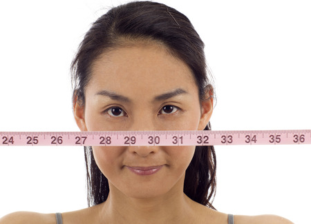 Asian woman with a measuring tape over her face isolated over white backgroundの写真素材