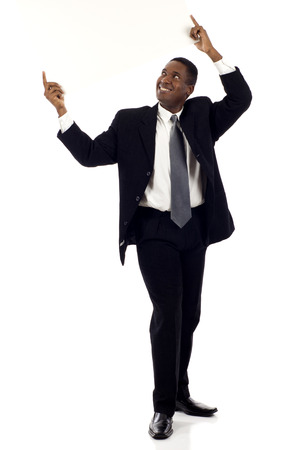 Full length a happy black businessman holding a blank sign above his head and looking at it  - isolated over white backgroundの写真素材