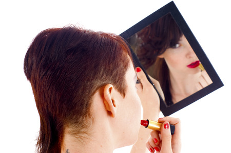 Young woman applying lipstick in front of mirror isolated over whiteの写真素材