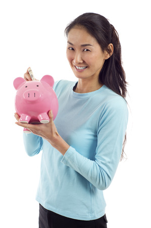 Happy Asian woman putting money in piggy bank isolated over white backgroundの写真素材