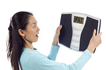 Asian woman looking surprised at her weight, Digital scale displaying the word " FAT"  isolated over white backgroundの写真素材