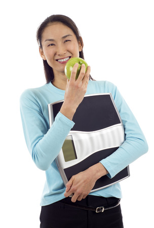 Smiling Asian woman holding an apple and a weight isolated over white backgroundの写真素材