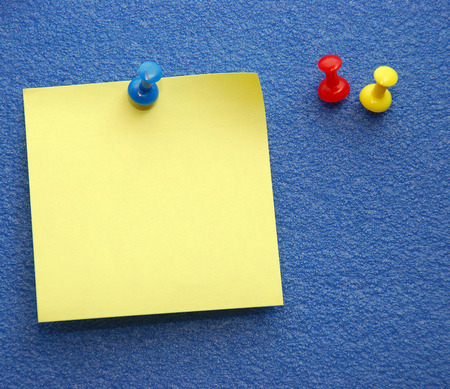 A yellow notepaper pinned on a blue board plus red and yellow extra pins at the side.