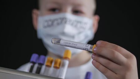 Boy is holding a metal suitcase. Child examines a medical test tube with a sample for the virus. Boy is careful of the virus. Pandemic March 2020. Coronavirus. COVID-19の写真素材