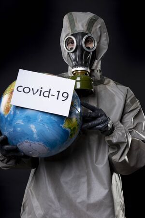 Man in a chemical protection suit and a gas mask. The guy is holding a model of the Earth, a globe....