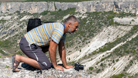 An adult man on the edge of the gorge, side view, is on all fours. Man over the gorge.