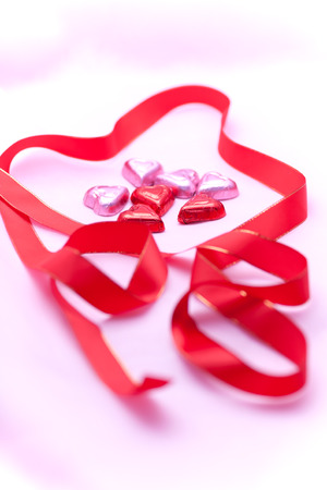 Red ribbon and heart-shaped chocolate with soft shadowsの写真素材