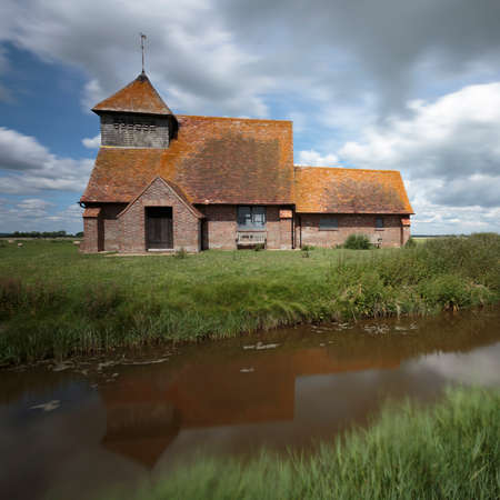 The church of St Thomas Ã  Becket reflected in a canal near Brookland, Romney Marsh, Englandの写真素材