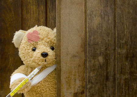 Teddy bear with bandages and thermometer on wood background with copy space.の写真素材