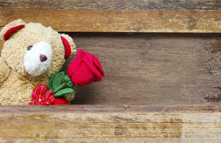 Valentine's day concept with Cute teddy Bears toy clutching a red rose in its arms on wooden background for an anniversary or valentine's celebration, copy space.の写真素材