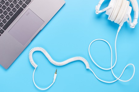 top view upon gadgets on blue background, the composition of a laptop and headphones with a wire in the shape of a heartの写真素材