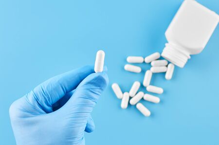 Young human hand hold pills tablets in palm. Healthcare, medical and pharmaceutical concept. Isolated on blue background. Close upの写真素材