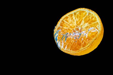Fresh orange falling in water with splash on black background.の写真素材