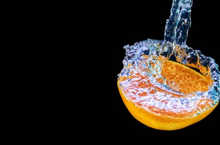 Fresh orange falling in water with splash on black background.の写真素材