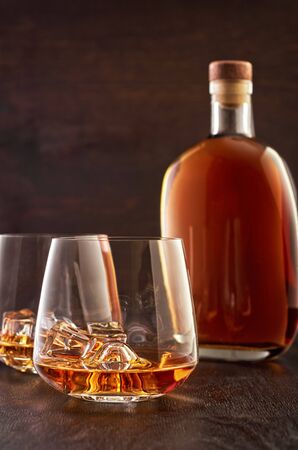 Two crystal glasses of whisky with ice on a wooden table. In the background is a full bottle of whiskey.の写真素材