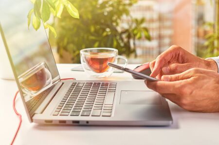 Men's hands do various work on a laptop against a window background on a bright sunny dayの写真素材
