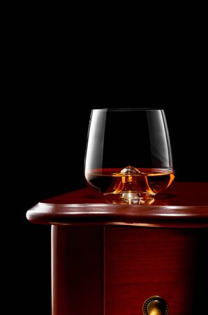 A glass of whiskey on a wooden table. Low key.