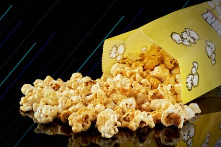 A paper bag with spilled popcorn on a dark background.の写真素材