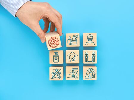 The concept of protection against COVID-19 coronavirus. Icons on wooden cubes indicate the necessary actions to prevent infection. A man's hand removes the cube with the virus icon.の写真素材