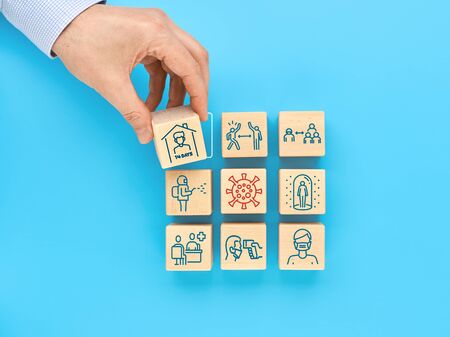The concept of protection against COVID-19 coronavirus. Icons on wooden cubes indicate the necessary actions to prevent infection. A man's hand adds a cube with a self-isolation icon.の写真素材
