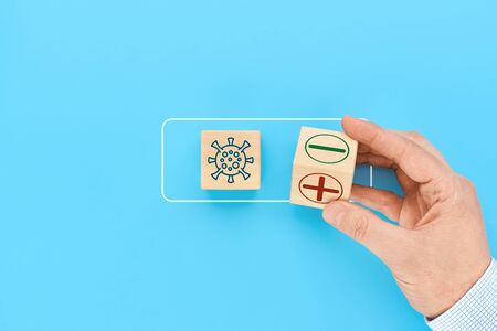 Concept for protection against COVID-19 coronavirus. A wooden cube in a man's hand shows a positive or negative test result for virus infection.の写真素材