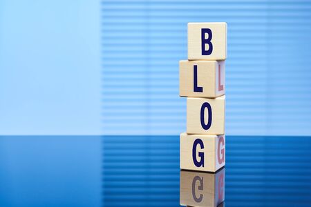 The inscription BLOG on wooden cubes standing on top of each other on a blue background with a reflection on the surface. Free space for text.の写真素材