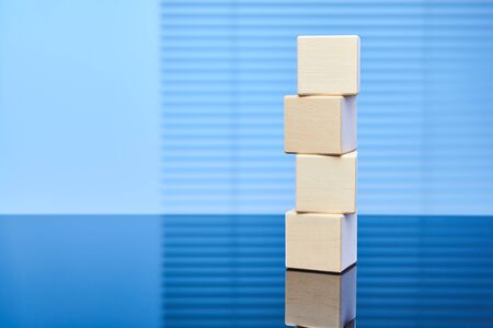 Four wooden cubes on a blue background are placed on top of each other. Business concept of the...