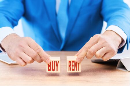 Business concept of choosing between renting and buying. The businessman holds cubes with the words BUY and RENT on each cube, respectively.の写真素材