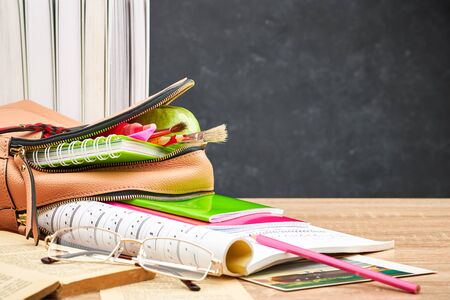 School backpack with colored notebooks and pencils, textbooks, sheet music, an Apple on a wooden...