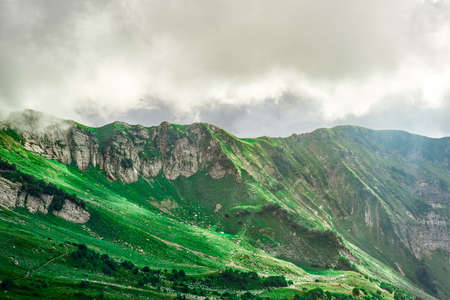 Landscape of mountain slopes covered with Alpine grass and shrouded in clouds with rays of warm evening light in Krasnaya Polyana, Sochi. Mountain Hiking.の写真素材