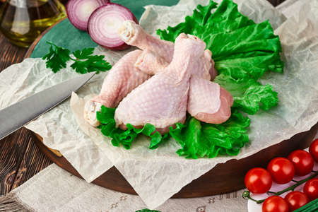 Fresh chicken drumstick on a cutting Board, on a dark wooden table with various kitchen utensils, spices, herbs and vegetables, cooking a chicken dish. Rustic still life.の写真素材
