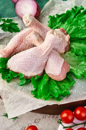Fresh chicken drumstick on a cutting Board, on a dark wooden table with various kitchen utensils, spices, herbs and vegetables, cooking a chicken dish. Rustic still life, top view.の写真素材