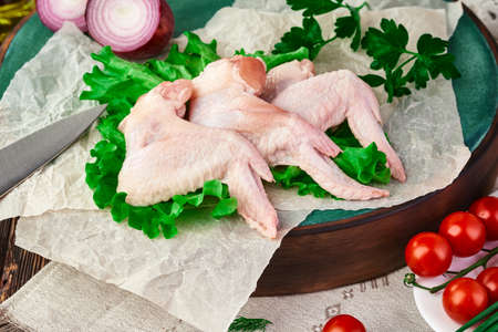 Fresh chicken wings on a cutting Board, on a dark wooden table with various kitchen utensils, spices, herbs and vegetables, cooking a chicken dish. Rustic still life.の写真素材