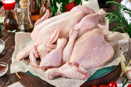 Chicken set of whole carcass, wings, leg and breast on a cutting Board, on a dark wooden table with various kitchen utensils, spices, herbs and vegetables, cooking chicken dishes. Rustic still lifeの写真素材