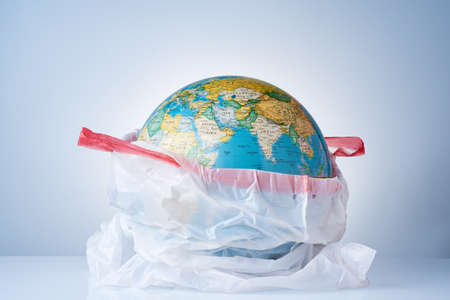The concept of protecting the world from plastic waste, fighting environmental pollution, fighting for the environment, a globe in a white garbage bag on a light background. No plastic bags.の写真素材