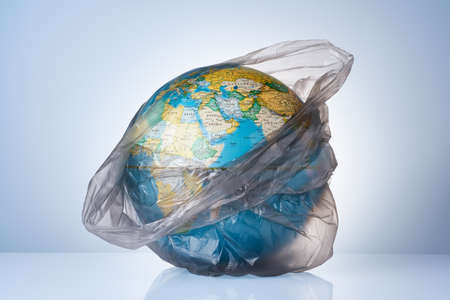 The concept of protecting the world from plastic waste, fighting environmental pollution, fighting for the environment, a globe in a black garbage bag on a light background. No plastic bags.の写真素材