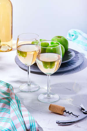 Still life of two glasses of white wine and a plate of green apples in the sunlight. Two glasses of wine on the table on a gray background.の写真素材