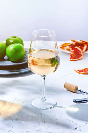 Still life of a large glass of white wine and a plate of green apples in the sunlight. A glass of wine on the table on a gray background.の写真素材