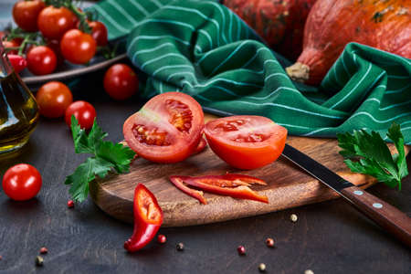 Two halves of a ripe red tomato on the table with the autumn harvest. Still life with the autumn harvest of vegetables.の写真素材