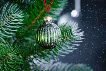 Christmas background with a spruce branch, a green ball on a branch and falling snow. New year's background with free space for text.の写真素材