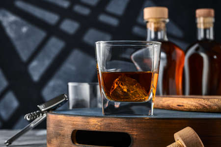 Square glass of whiskey with ice on a wooden tray, on a blue background. Two glasses of brandy and ice on a wooden tray, on a blue background.の写真素材