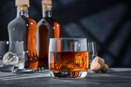 Round glass of whiskey with ice on a concrete table, on a blue background. Round glass of brandy with ice on a concrete table, on a blue background.の写真素材
