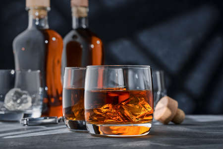 Two round glasses of whiskey with ice on a concrete table, on a blue background. Two round glasses of brandy on a concrete table, on a blue background.の写真素材