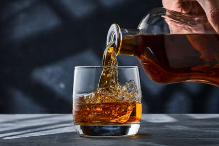 Round glass of whiskey with ice on a concrete table, a glass is filled with whiskey from a bottle. A glass of brandy with ice on a concrete table, brandy from a bottle is poured into the glass.の写真素材