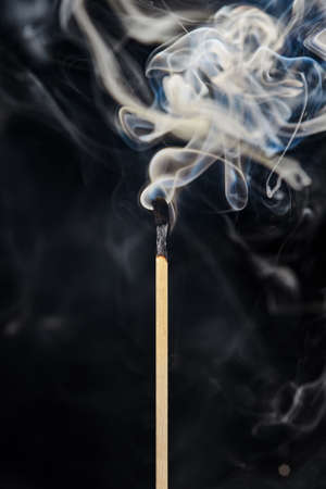 A single extinguished match with smoke rising up, isolated on a black background. Free space for text, layout for design.の写真素材