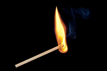 A single burning match with flames and smoke rising up, isolated on a black background. Free space for text, layout for design.の写真素材