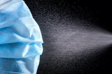 Spray on a medical mask to kill viruses, aerosol drops hit the protective mask. Concept of health...