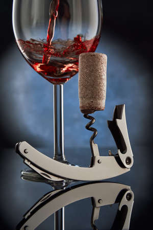 A corkscrew with a twisted wooden cork on the background of a glass of pouring red wine. Free space for text.の写真素材